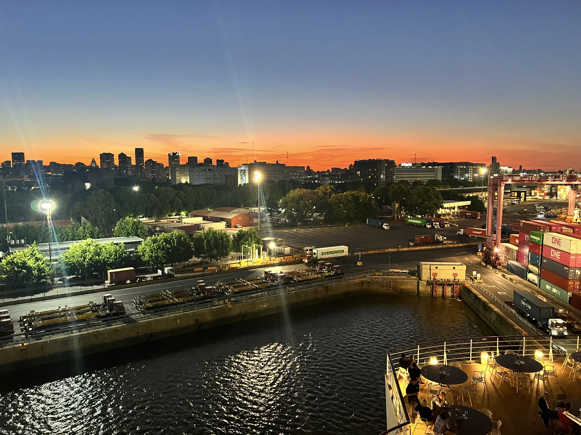 Blick vom Schiff auf eine Hafeneinfahrt in der goldenen Stunde, der Himmel leuchtet warm über der Stadt.