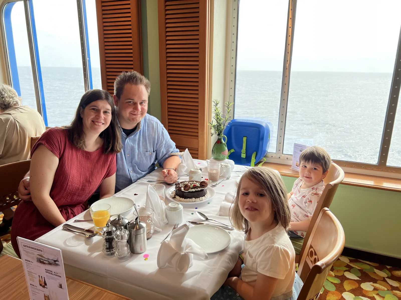 Familie am gedeckten Restauranttisch an Bord, dahinter das Meer.