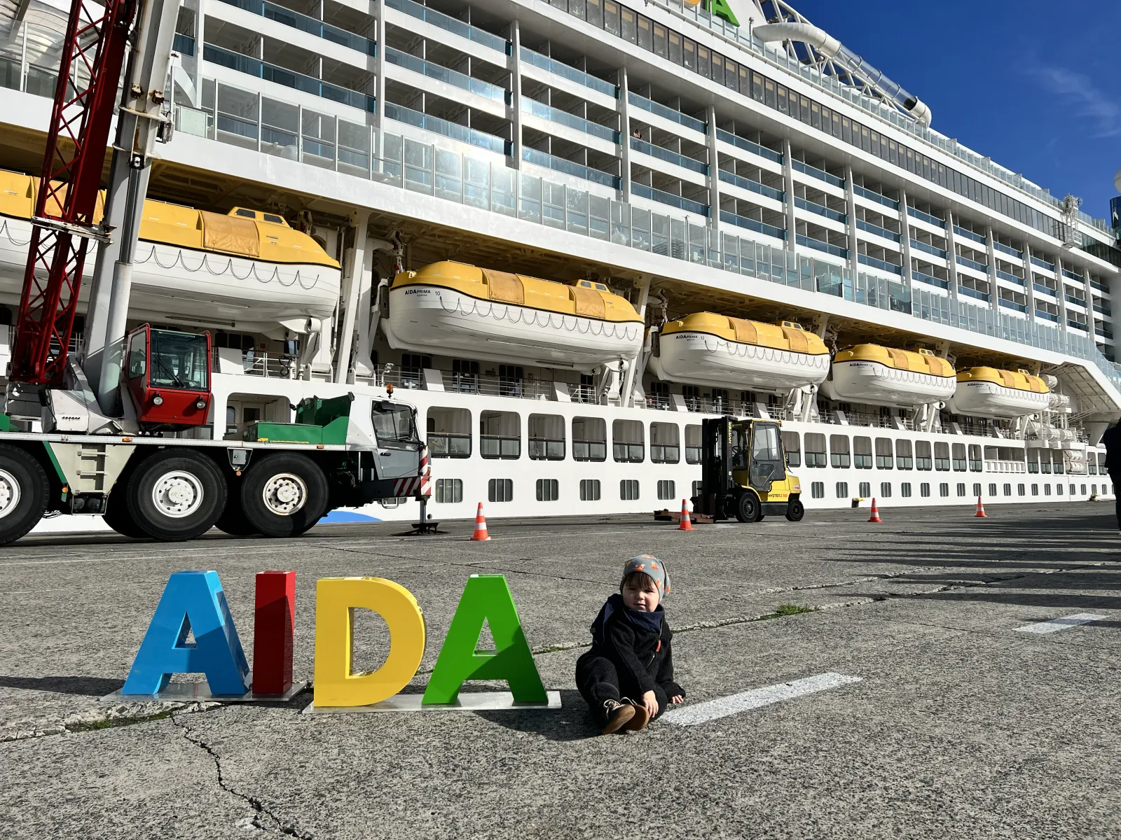 Kleinkind zwischen den bunten AIDA-Buchstaben am Pier vor dem Schiff.