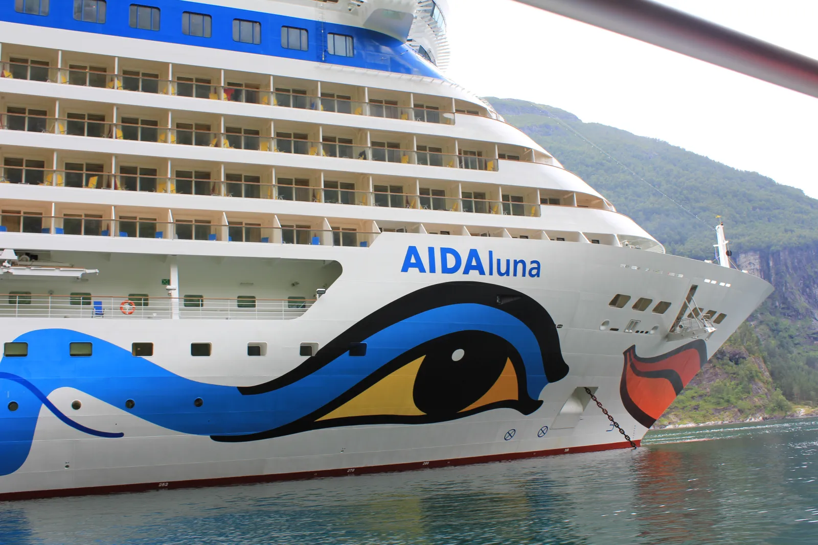 Bug der AIDAluna mit Auge und Kussmund vor einer Fjordkulisse.